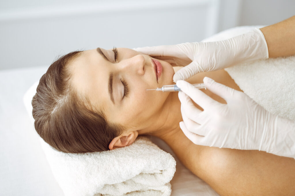 Beautician doing beauty procedure with syringe to face of young brunette woman. Cosmetic medicine and surgery, beauty injections