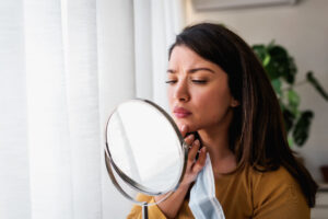 Woman checking her skin in mirror, likely suffering from hormone-related skin issues