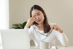Tired woman wiping her eyes at work, suffering from hormonal imbalance fatigue.