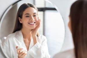 Woman smiling to herself in the mirror and touching her face after receiving a chemical peel or Hydrafacial.