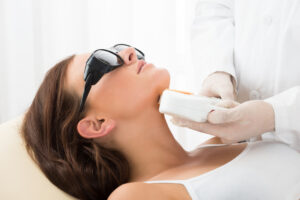 Close-up of a patient receiving Lumecca IPL skin treatment from her provider on her face and jaw.
