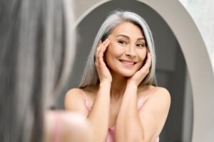 Older woman smiling happily in mirror after pairing Botox with other aesthetic treatments.