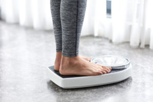 Close-up of a woman standing on a scale and weighing herself, suffering from hormonal weight gain.